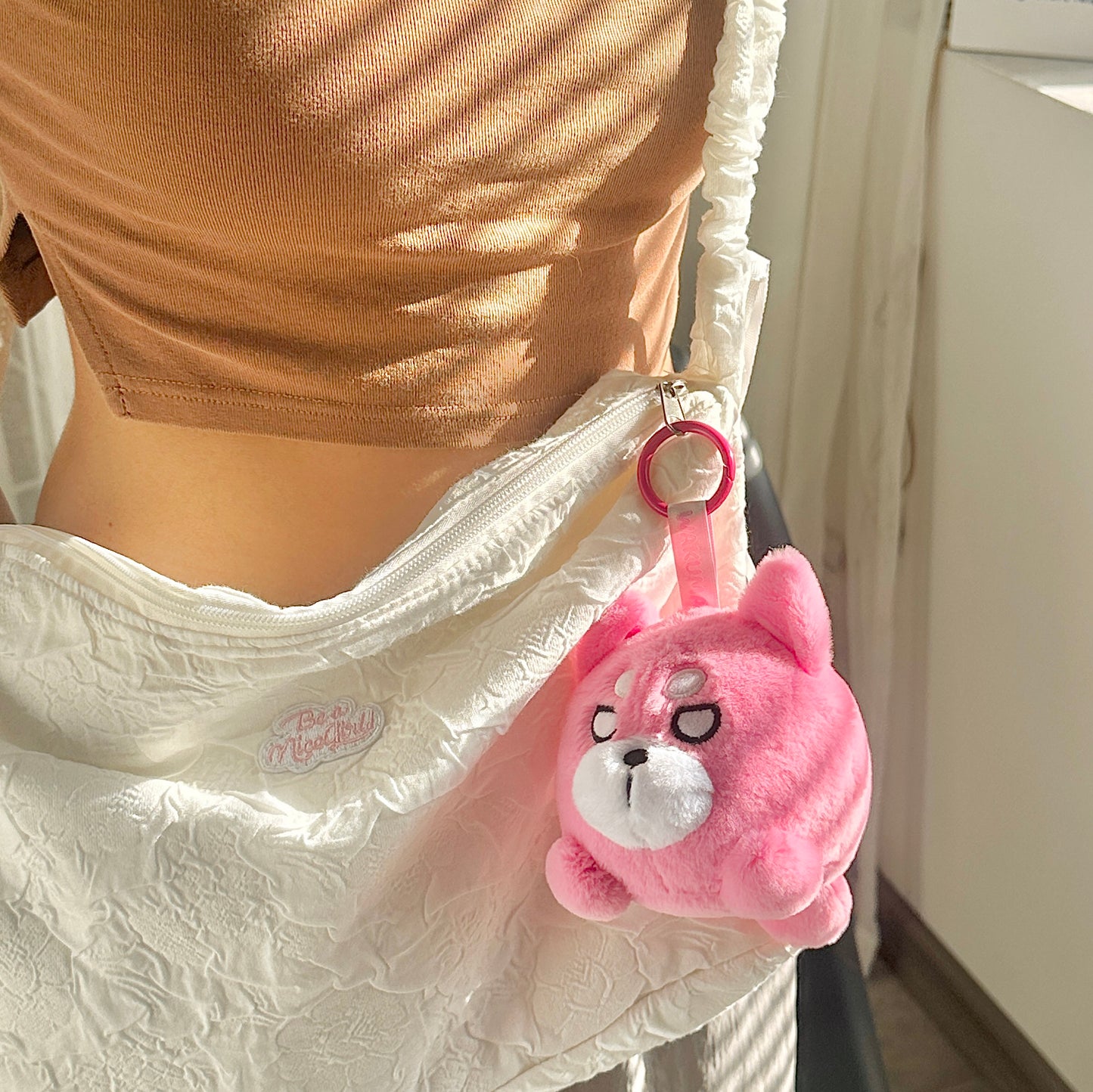 Pink round Wakuma bear plush keychain on bag zipper.