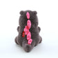 Grey kaiju baby plush toy viewed from behind, showing pink spikes along its back and tail on a white background.